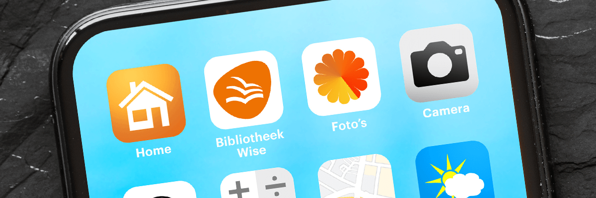 Foto van een telefoon met op het startscherm onder andere de app Bibliotheek Wise Telefoon met meerdere apps waaronder de vernieuwde app Bibliotheek Wise
