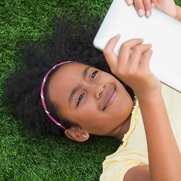 Afbeelding van een kind dat buiten op een tablet leest